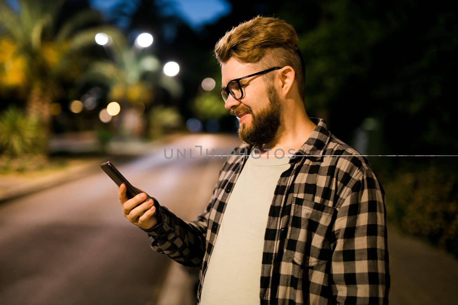 Man waits taxi by using transportation app on night street. Technologies and city