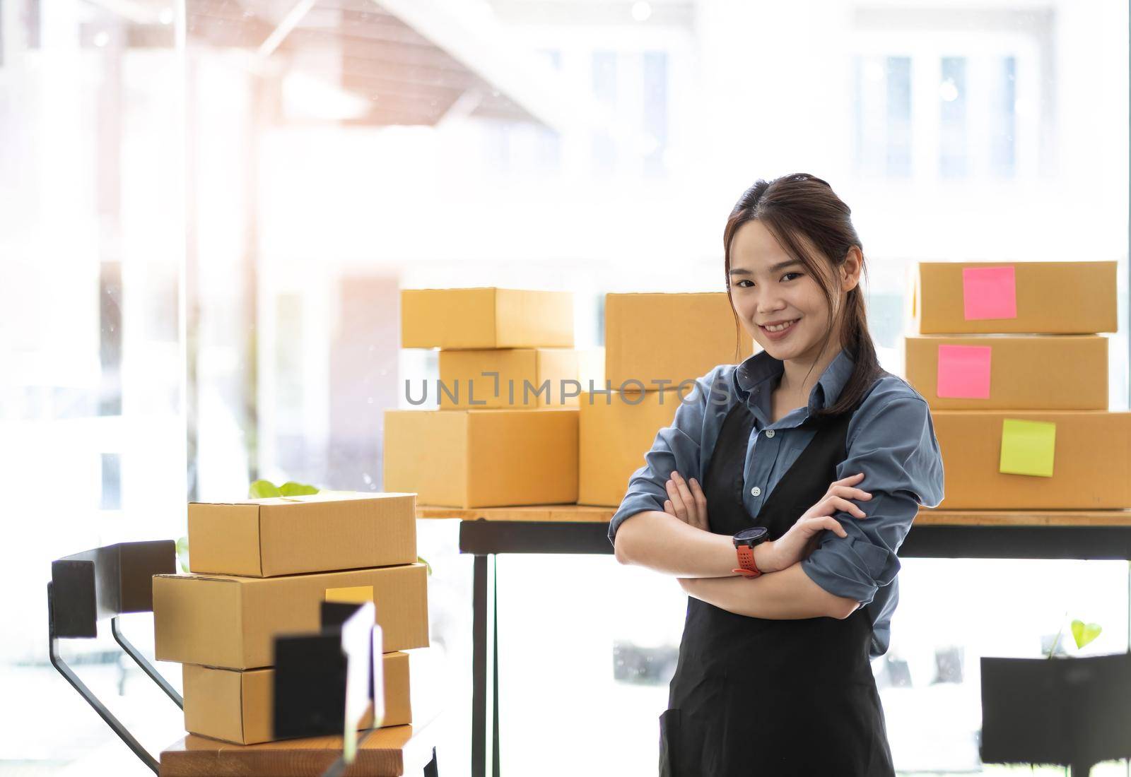 Young attractive asian woman owner startup business look at camera work happy with box at home prepare parcel delivery in sme supply chain by wichayada
