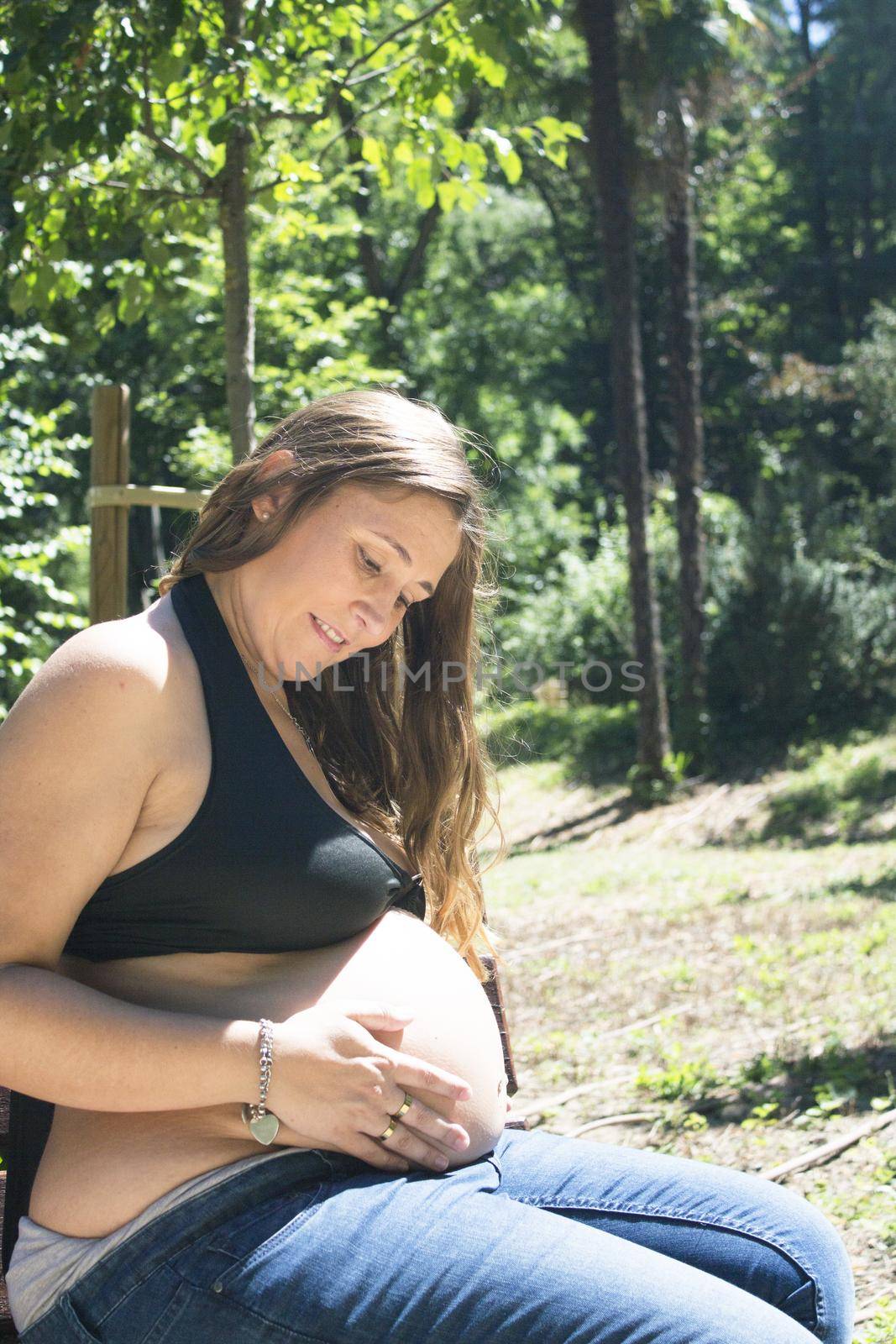 Seven month pregnant woman in a park dressed in jeans