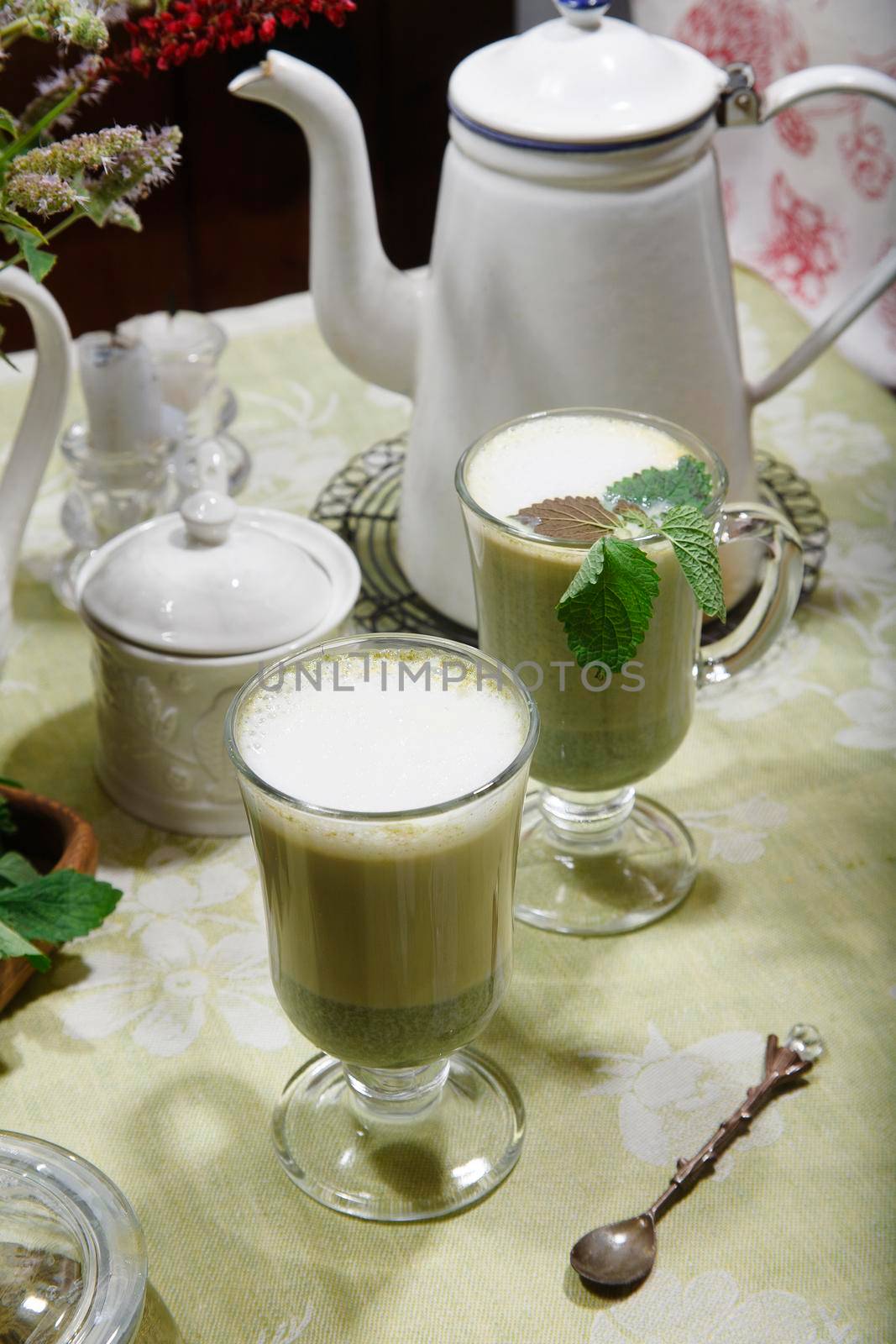 Matcha green tea in two glass cups with mint leaves on green table cloth, summer breakfast concept, selective focus.