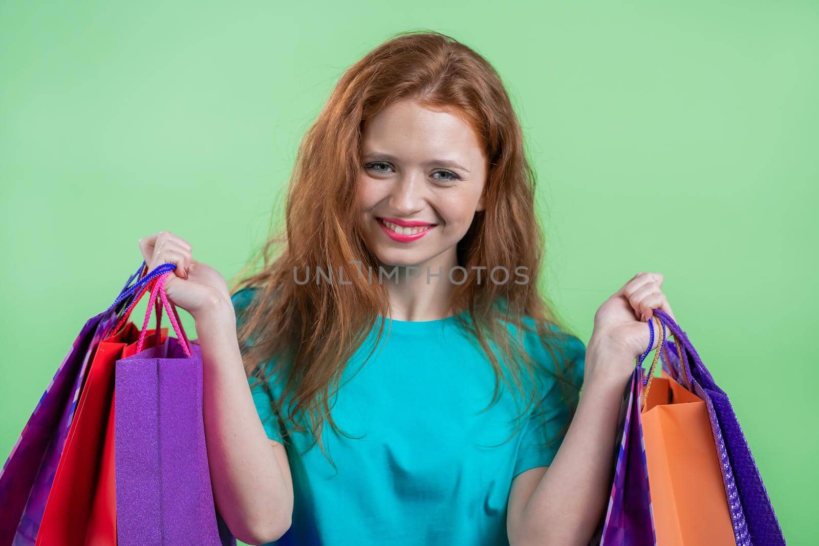 Excited woman with colorful paper bags after shopping on green studio background. Concept of seasonal sale, purchases, spending money on gifts by kristina_kokhanova