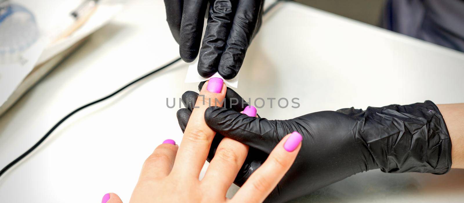 Manicurist applies a matte coating with a napkin on female pink nails in a nail salon