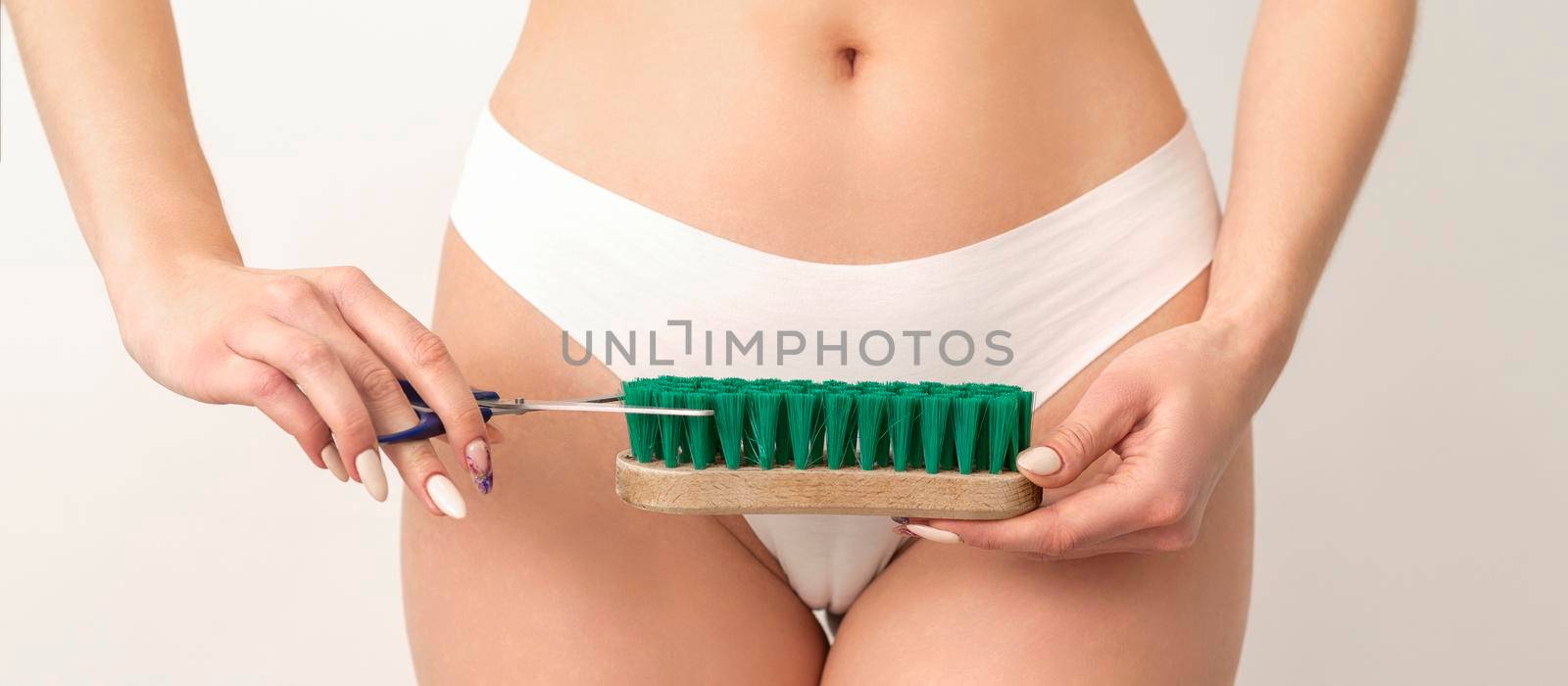 Epilation concept. A young caucasian woman wears white panties is cutting a cleaning brush with scissors standing on white background