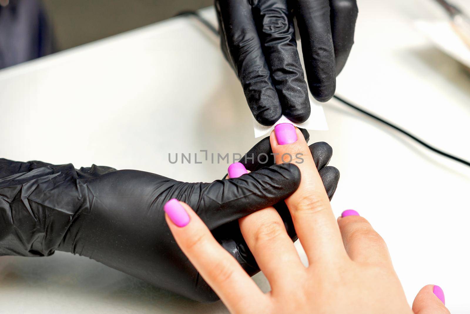 Manicurist applies a matte coating with a napkin on female pink nails in a nail salon