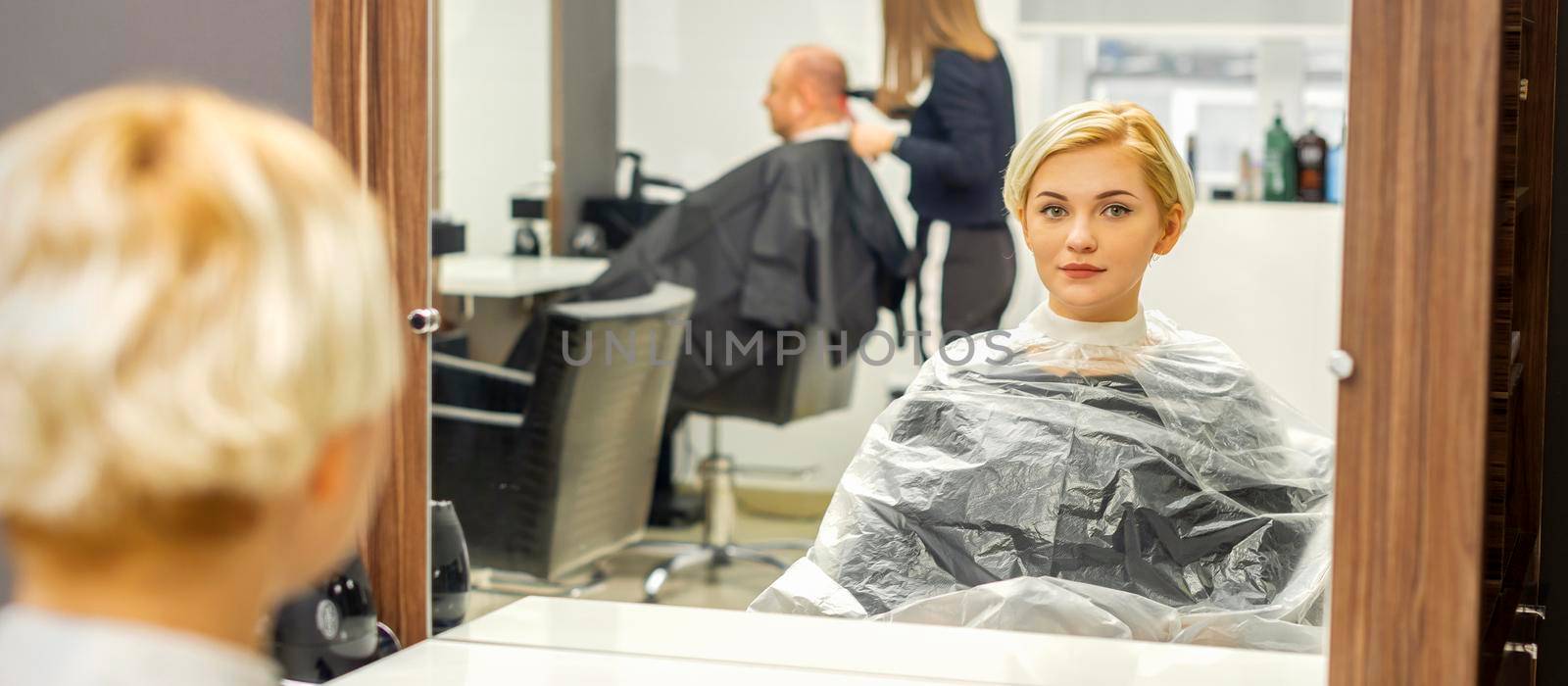 Young female client waiting for the hairdresser looking in the mirror in a hair salon