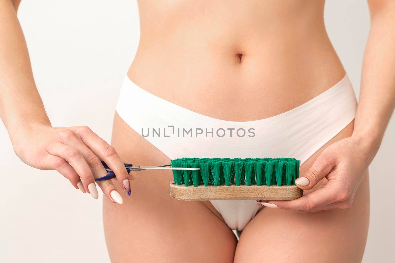 Epilation concept. A young caucasian woman wears white panties is cutting a cleaning brush with scissors standing on white background