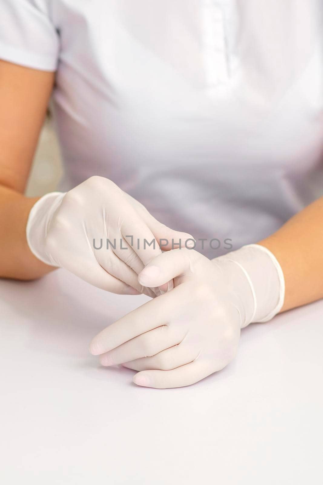Two hands in white protective gloves of nurse or female doctor sitting at the white table