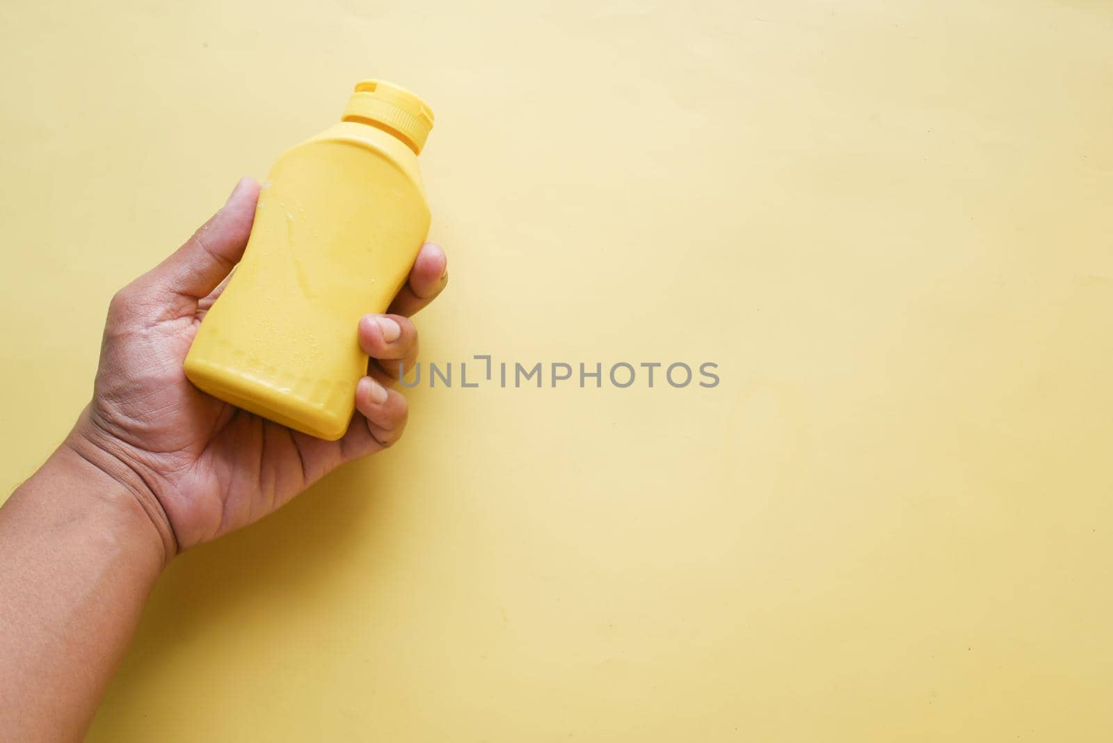 holding a mustard mayonnaise container on yellow background ,