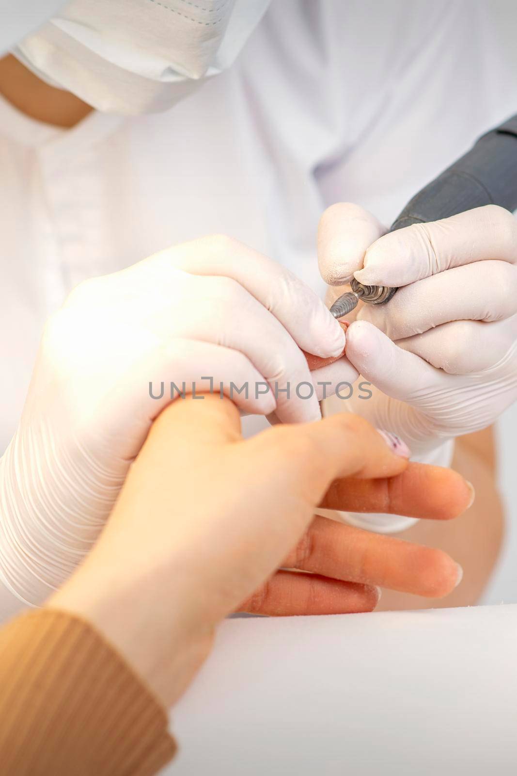 Closeup of manicure master removes nail polish uses an electric nail file in a nail salon