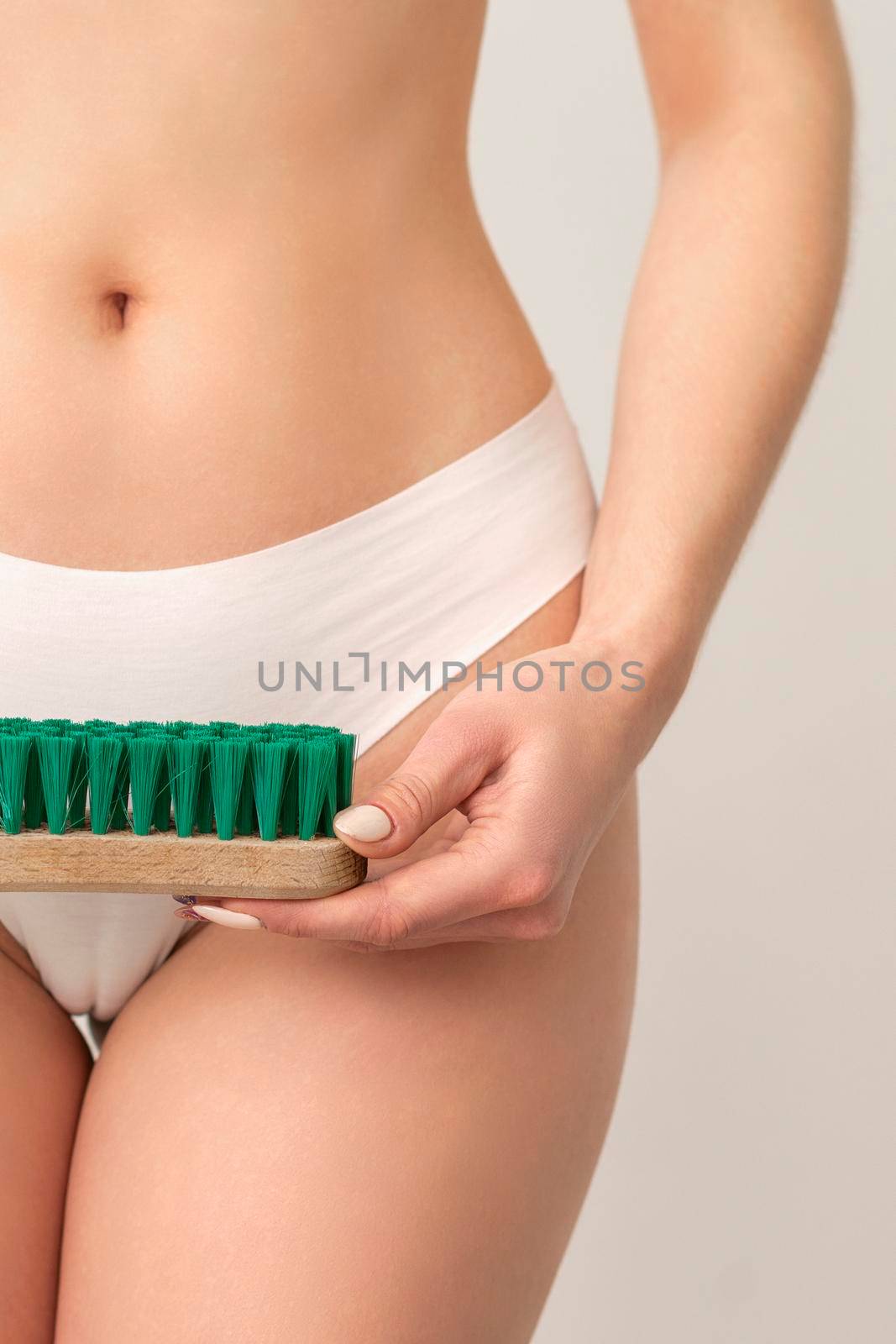 Epilation concept. A young caucasian woman wears white panties is holding a cleaning brush standing on white background