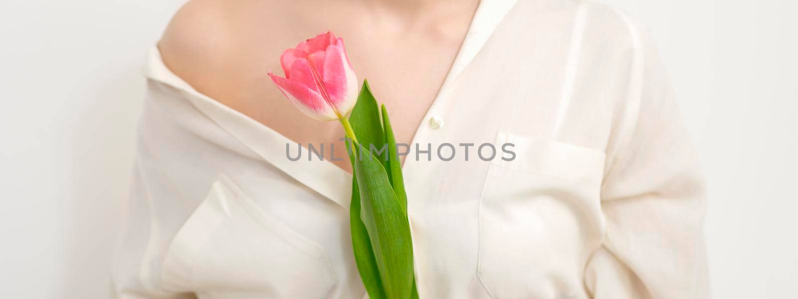 Beautiful young unrecognizable female with one tulip against a white background
