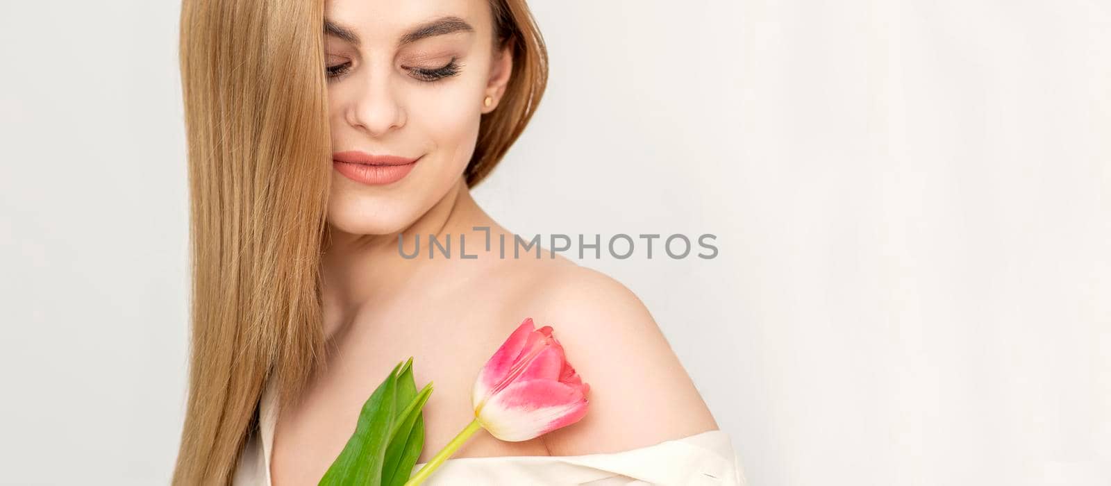 Beautiful caucasian young woman with one tulip looking on a flower against a white background