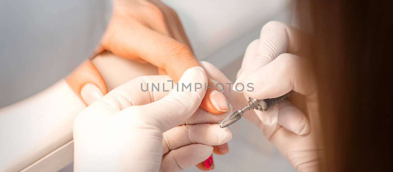 Closeup of manicure master removes nail polish uses an electric nail file in a nail salon