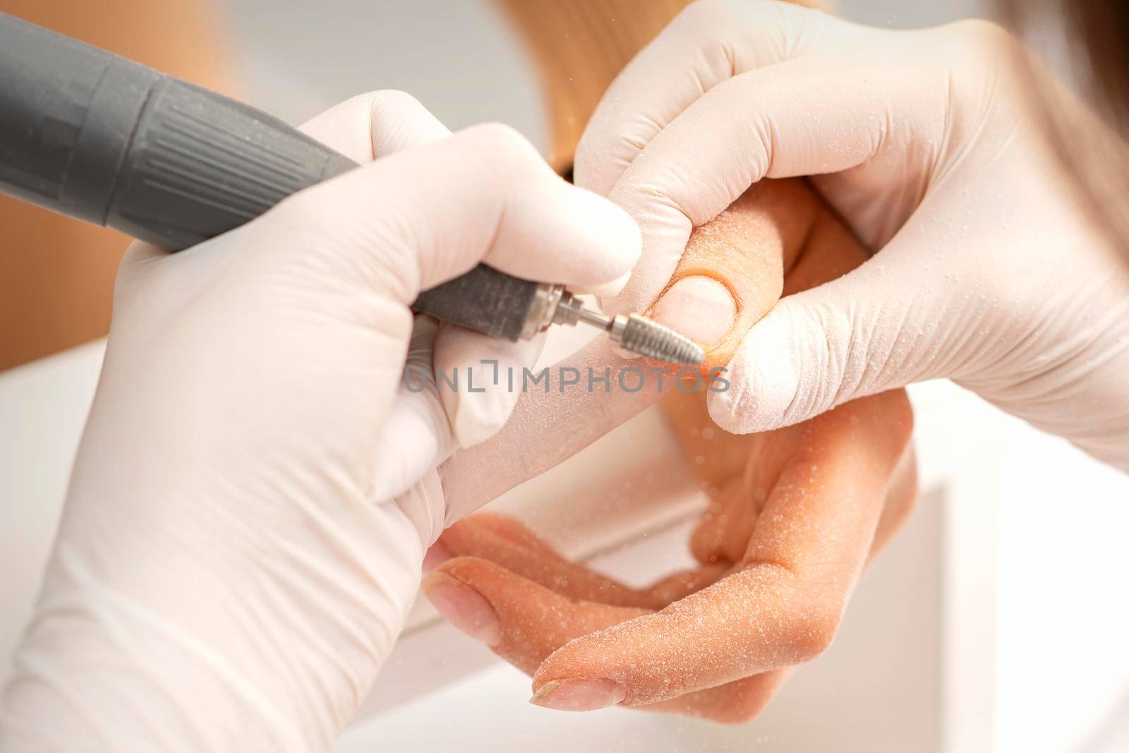 Closeup of manicure master removes nail polish uses an electric nail file in a nail salon