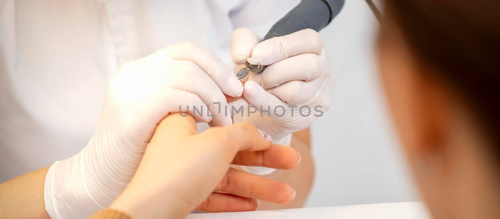 Closeup of manicure master removes nail polish uses an electric nail file in a nail salon