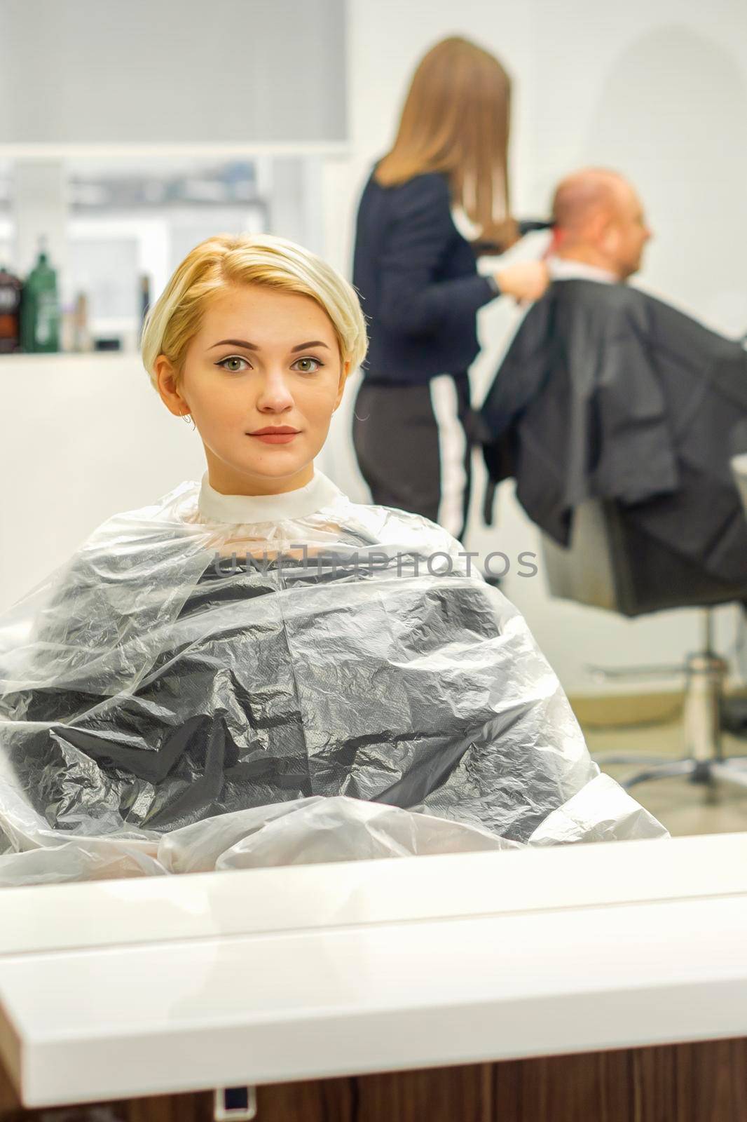 Young female client waiting for the hairdresser looking in the mirror in a hair salon