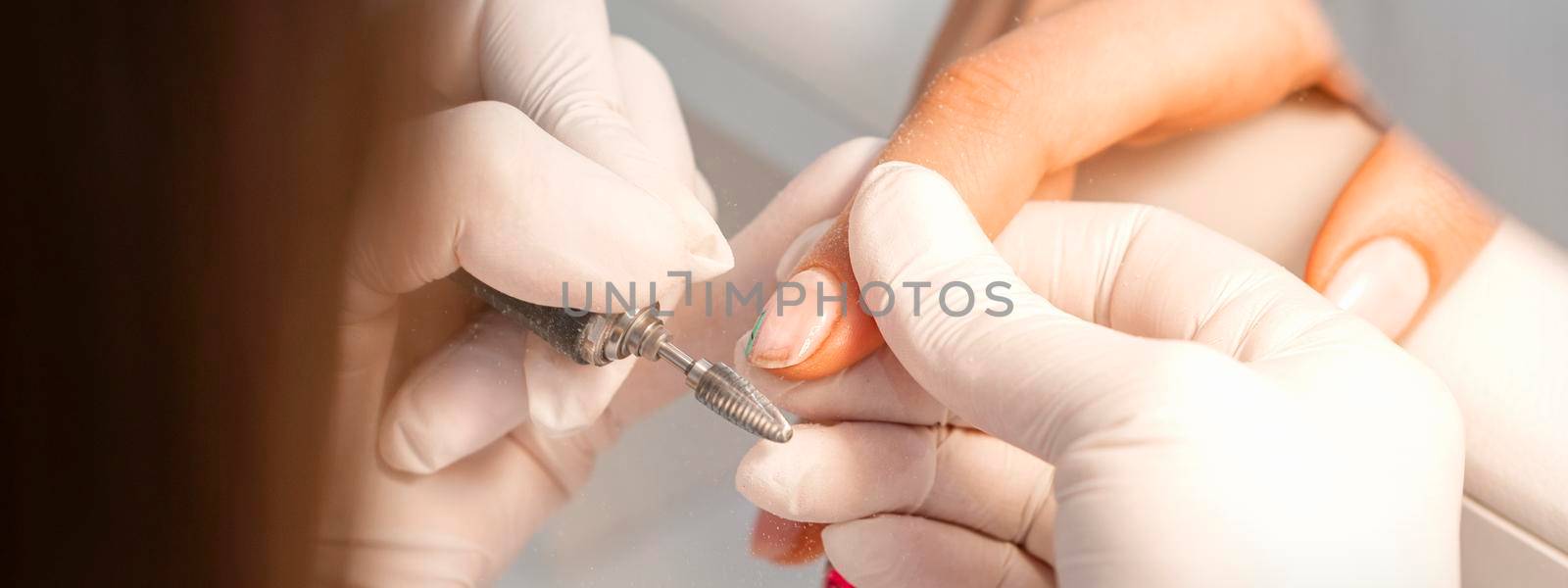 Closeup of manicure master removes nail polish uses an electric nail file in a nail salon