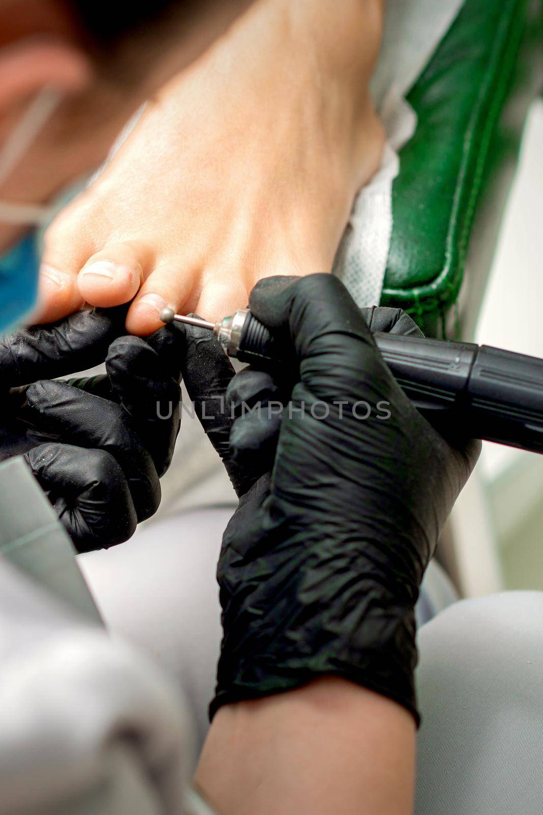 Pedicure master removes corns and cuticles with electric file machine on female toes in a nail salon