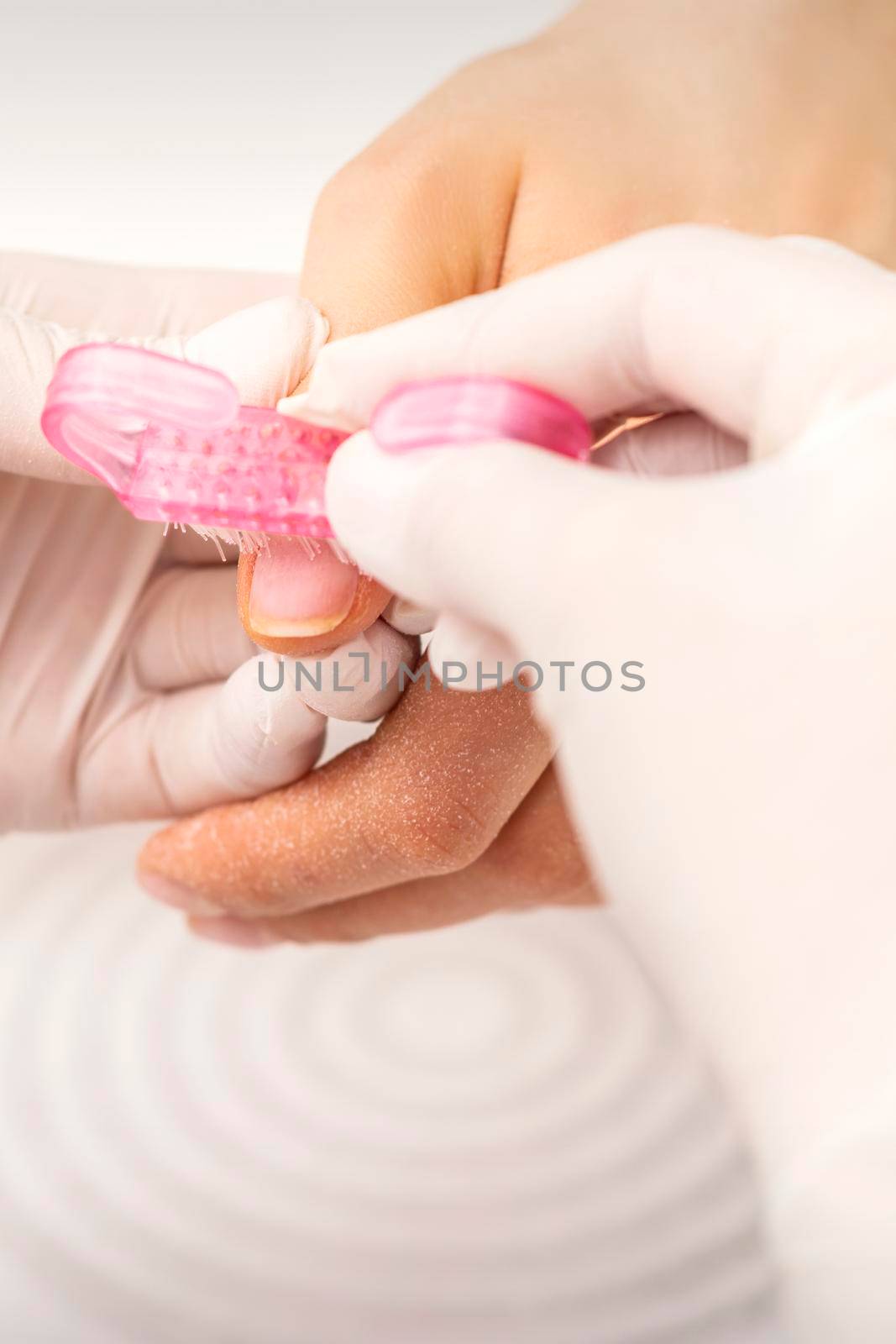 Closeup of manicurist is brushing dust with a pink plastic brush from female fingernails in a nail salon