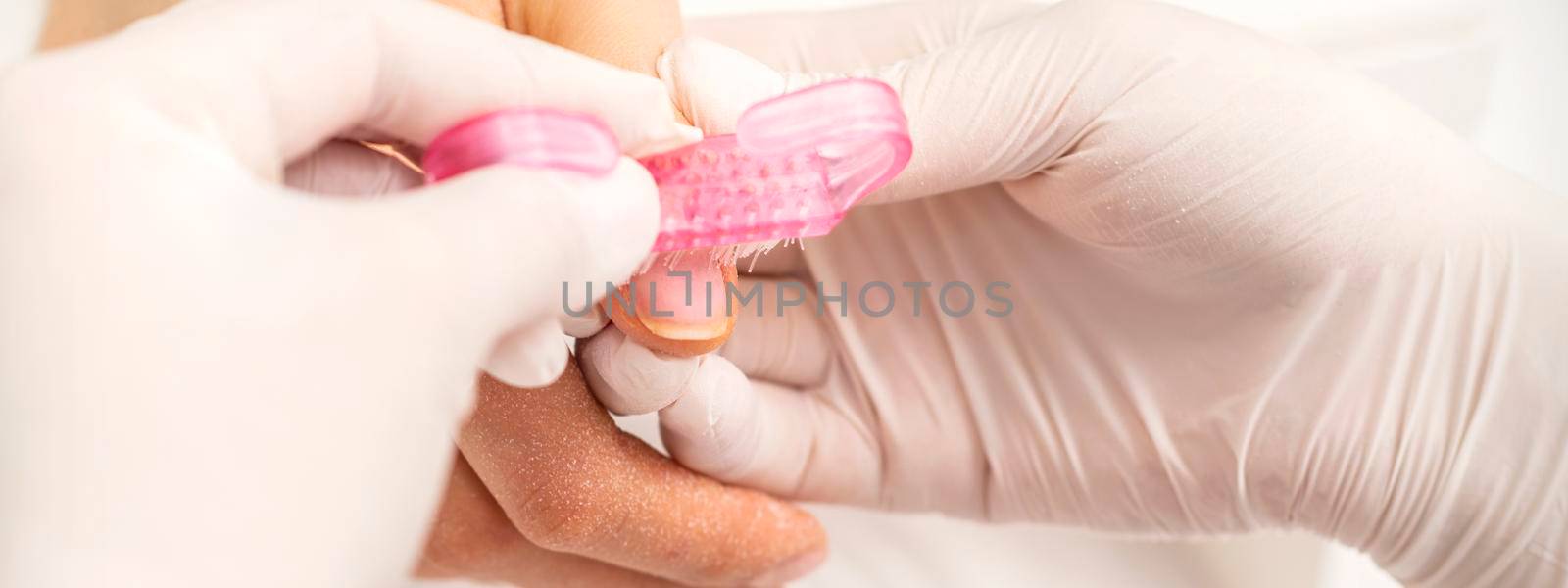 Closeup of manicurist is brushing dust with a pink plastic brush from female fingernails in a nail salon