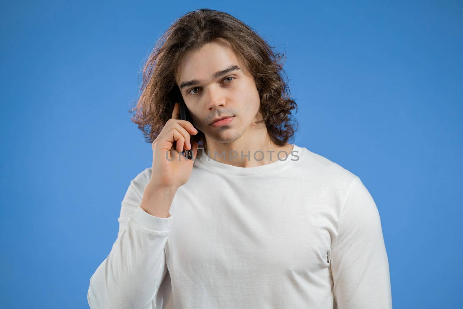 Young man speaks on phone. Guy holding and using smart phone. Blue studio background. High quality photo