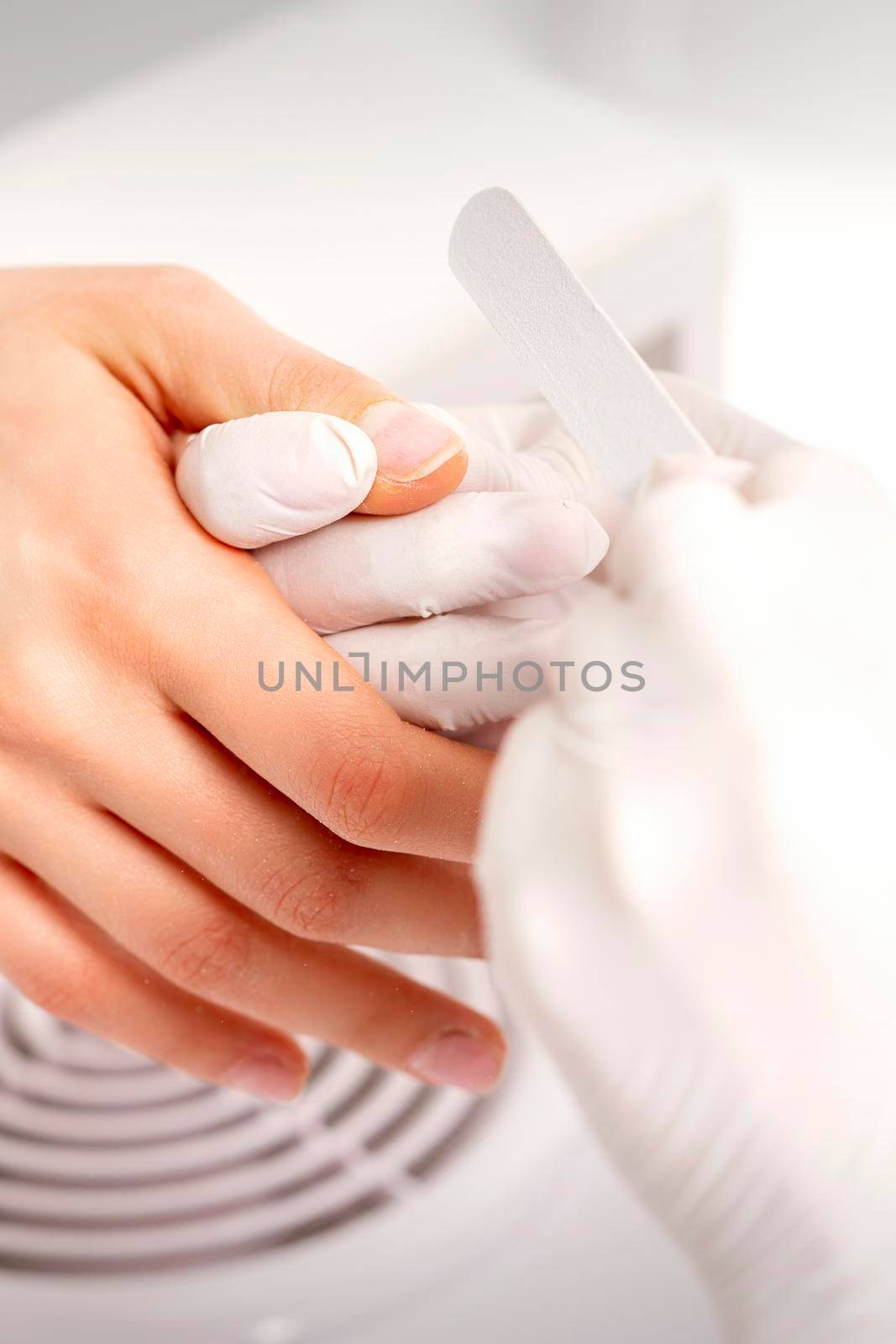 Manicure master wears white gloves with nail file doing manicure on female fingernails in a nail salon