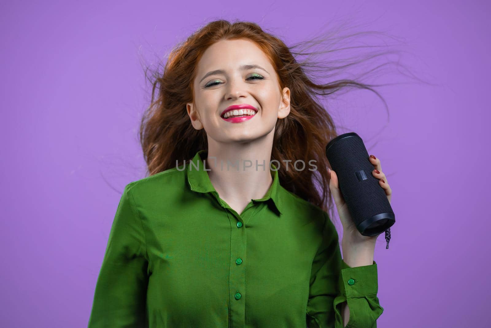 Woman listening to music by wireless portable speaker - modern sound system. Lady dancing, enjoying on violet studio background. She moves to the rhythm of music. by kristina_kokhanova