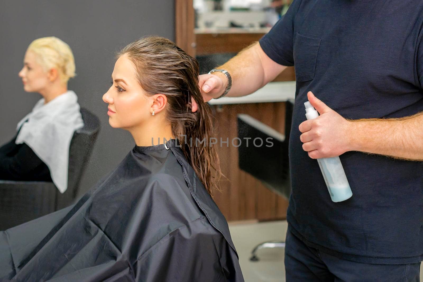 Male hairdresser sprays water long wet hair of a young woman in a hair salon