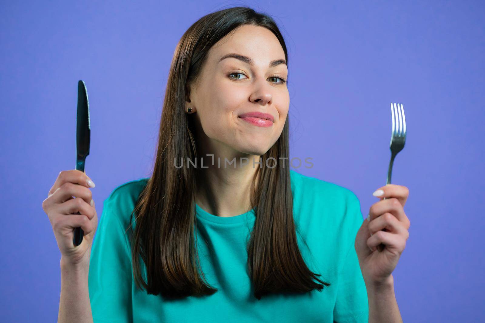 Portrait of hungry woman with fork and knife. Lady waiting for serving dinner dishes with cutlery on violet studio background. by kristina_kokhanova
