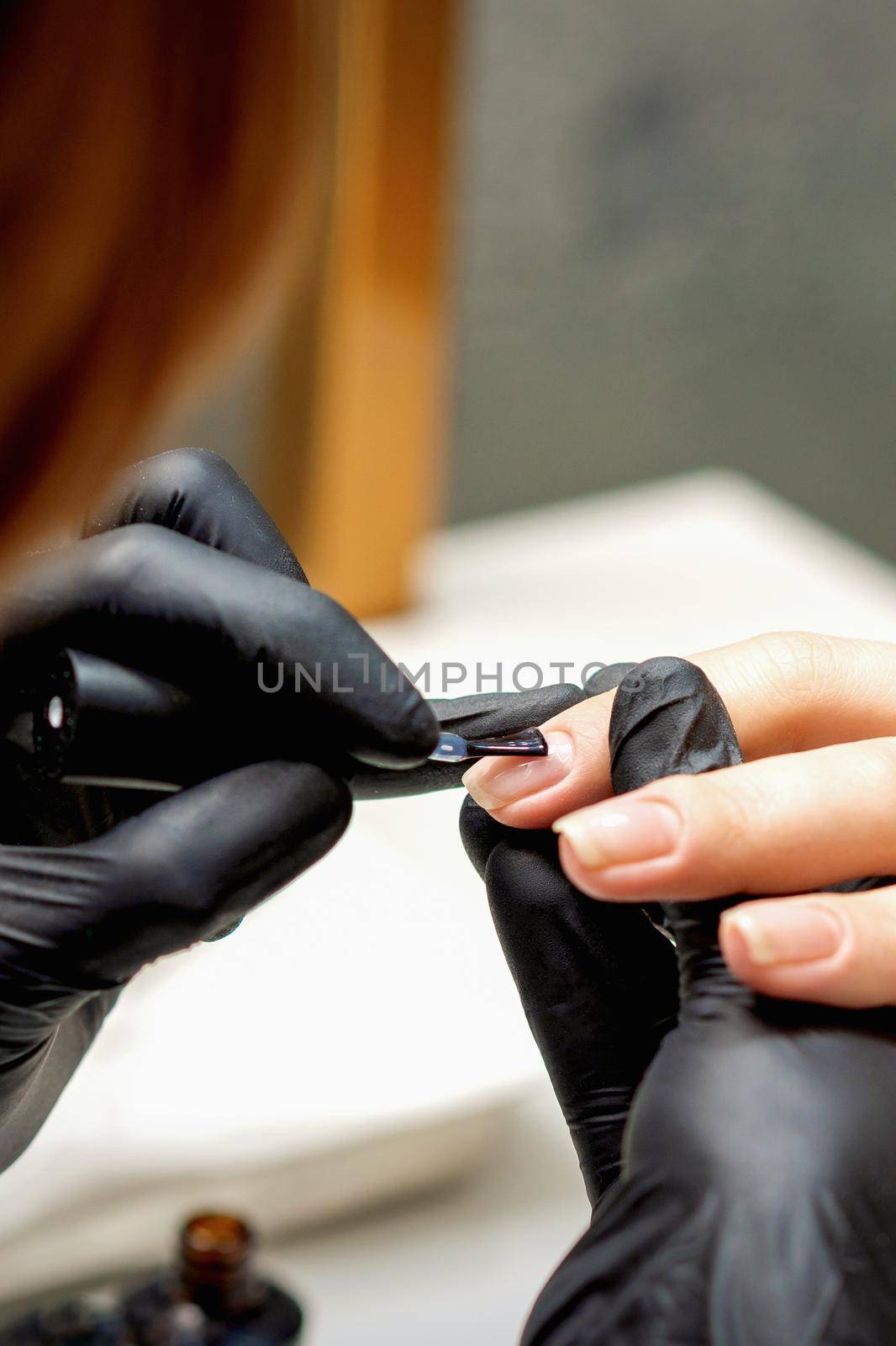 Close up of manicure master covering nails with the transparent polish of female nails in a nail salon