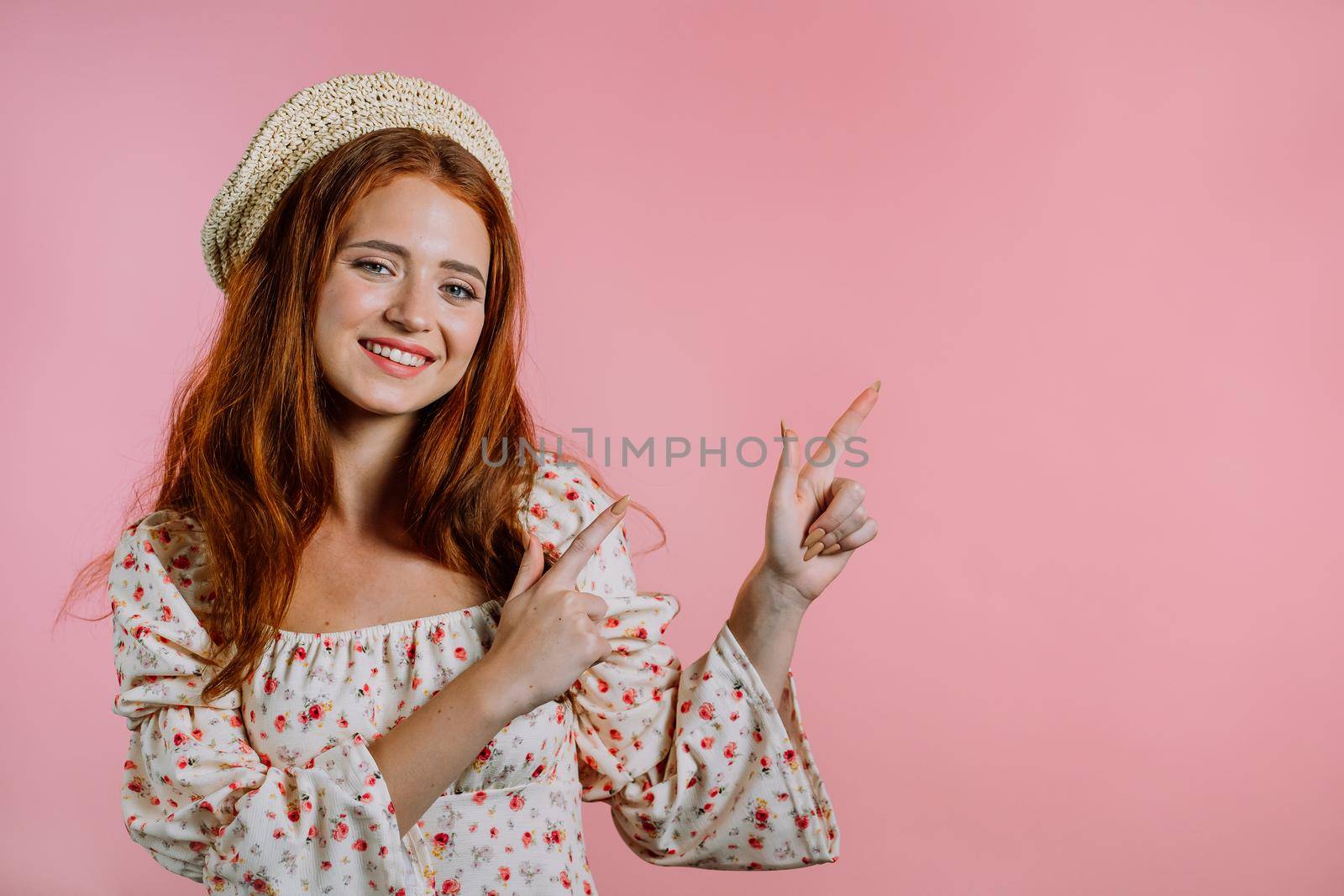 Happy smiling woman presenting and showing something isolated on pink background. Portrait of girl, she pointing with arms on her left with copy space. High quality photo