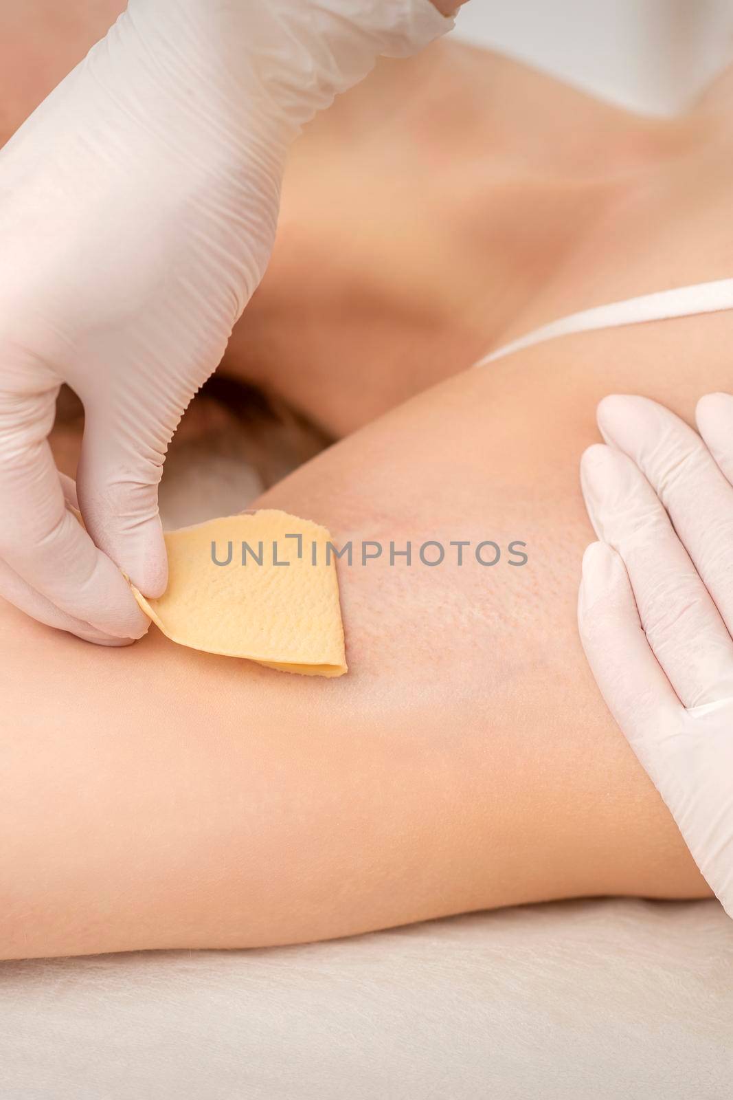 Close up of hands in gloves of beautician waxing young female armpit with sugar paste in hair removal salon