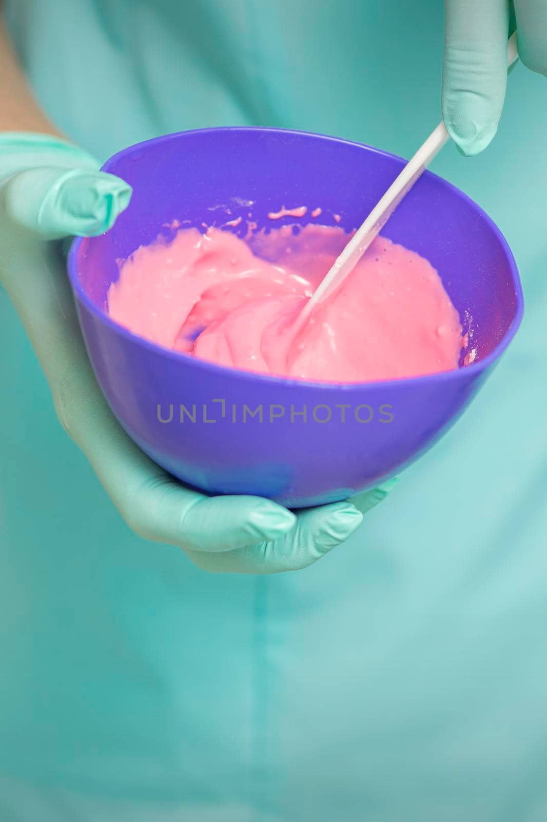 Close up of beautician's hands prepares pink alginate mask mixing in the blue bowl