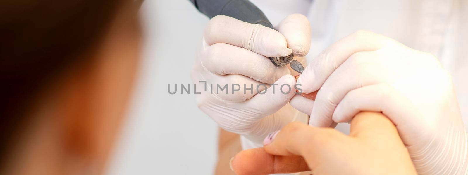 Closeup of manicure master removes nail polish uses an electric nail file in a nail salon