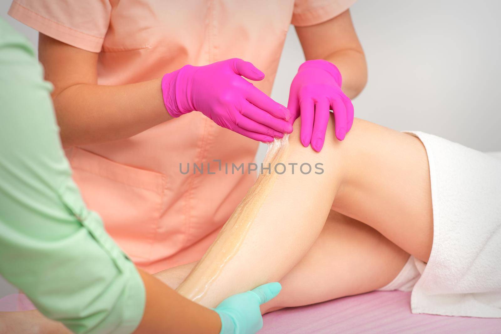 Hands of a beautician in pink gloves epilating leg of a young female in hair removal salon