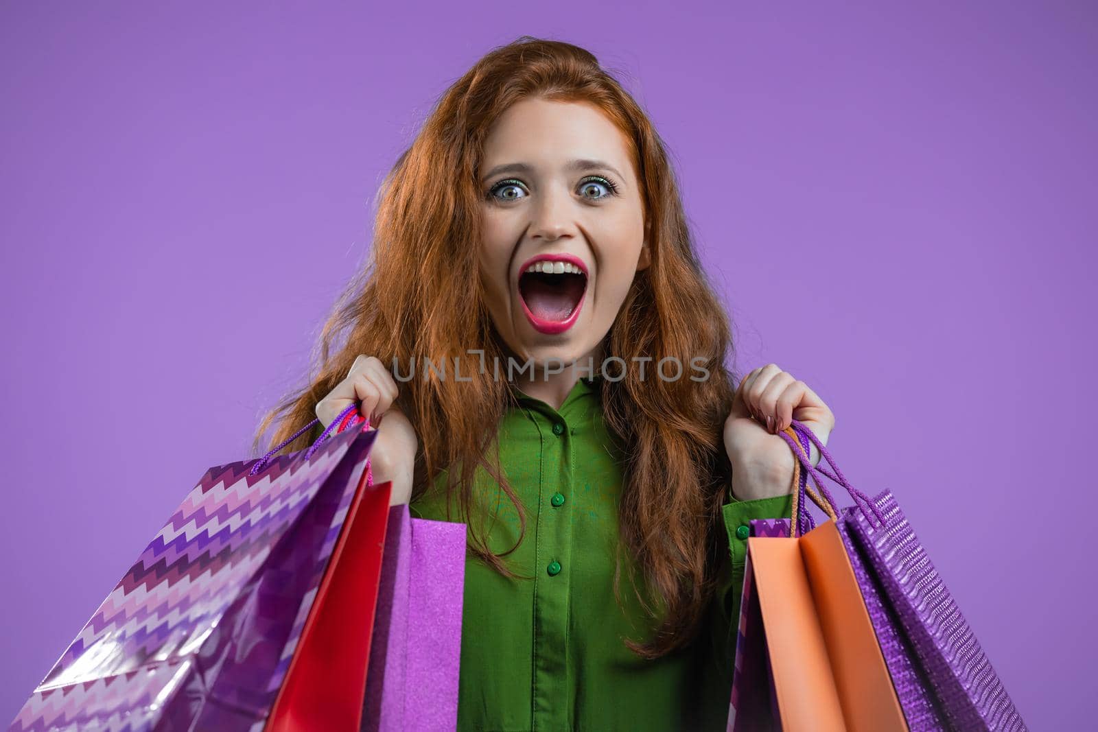 Excited woman with colorful paper bags after shopping on violet studio background. Concept of seasonal sale, purchases, spending money on gifts by kristina_kokhanova