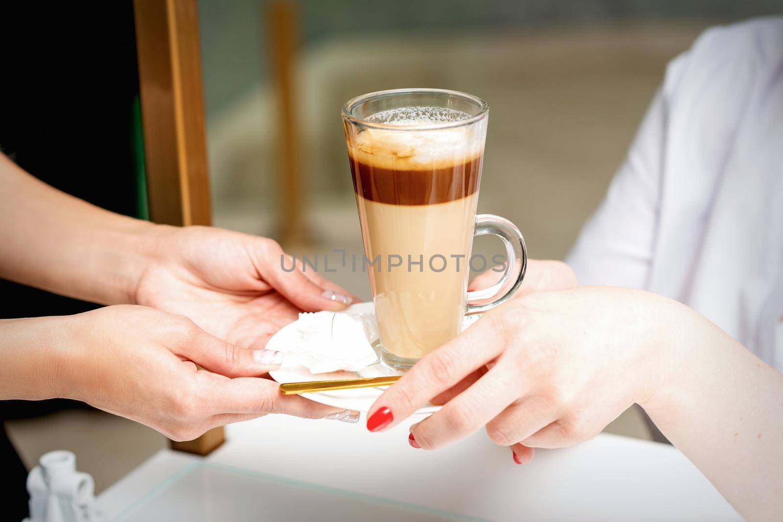 Closeup of woman's hands taking the latte cup from hands of a barista in a coffee shop