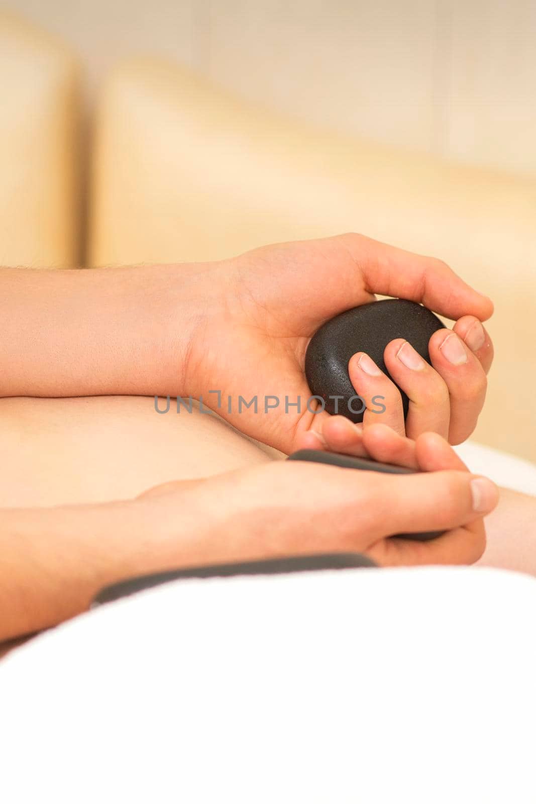 Hands of masseur hold black hot stones massaging back of a young adult woman in spa salon