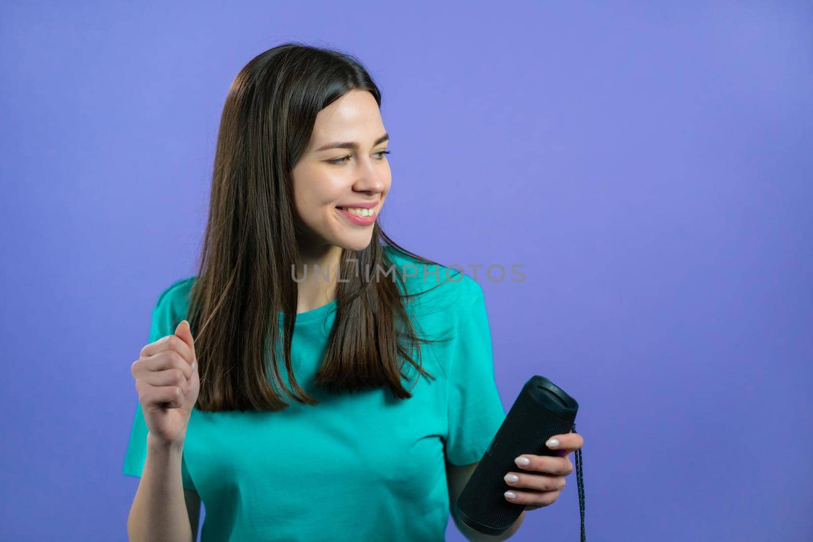 Woman listening to music by wireless portable speaker - modern sound system. Lady dancing, enjoying on violet studio background. She moves to the rhythm of music. High quality photo