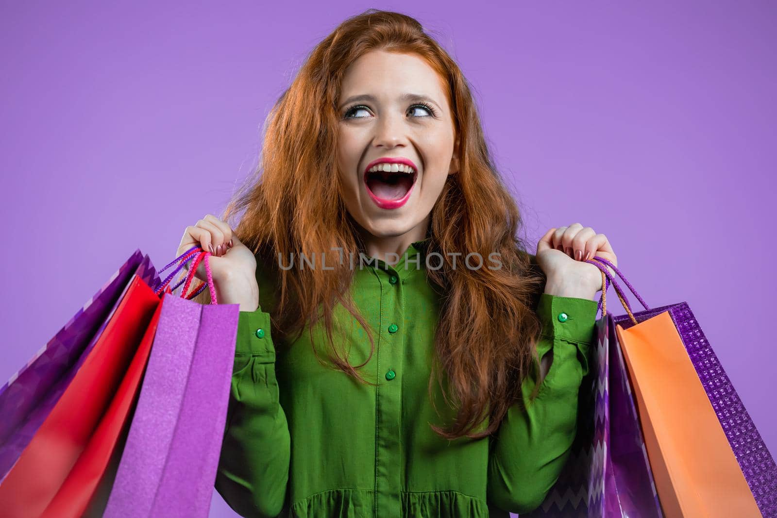 Excited woman with colorful paper bags after shopping on violet studio background. Concept of seasonal sale, purchases, spending money on gifts. High quality photo
