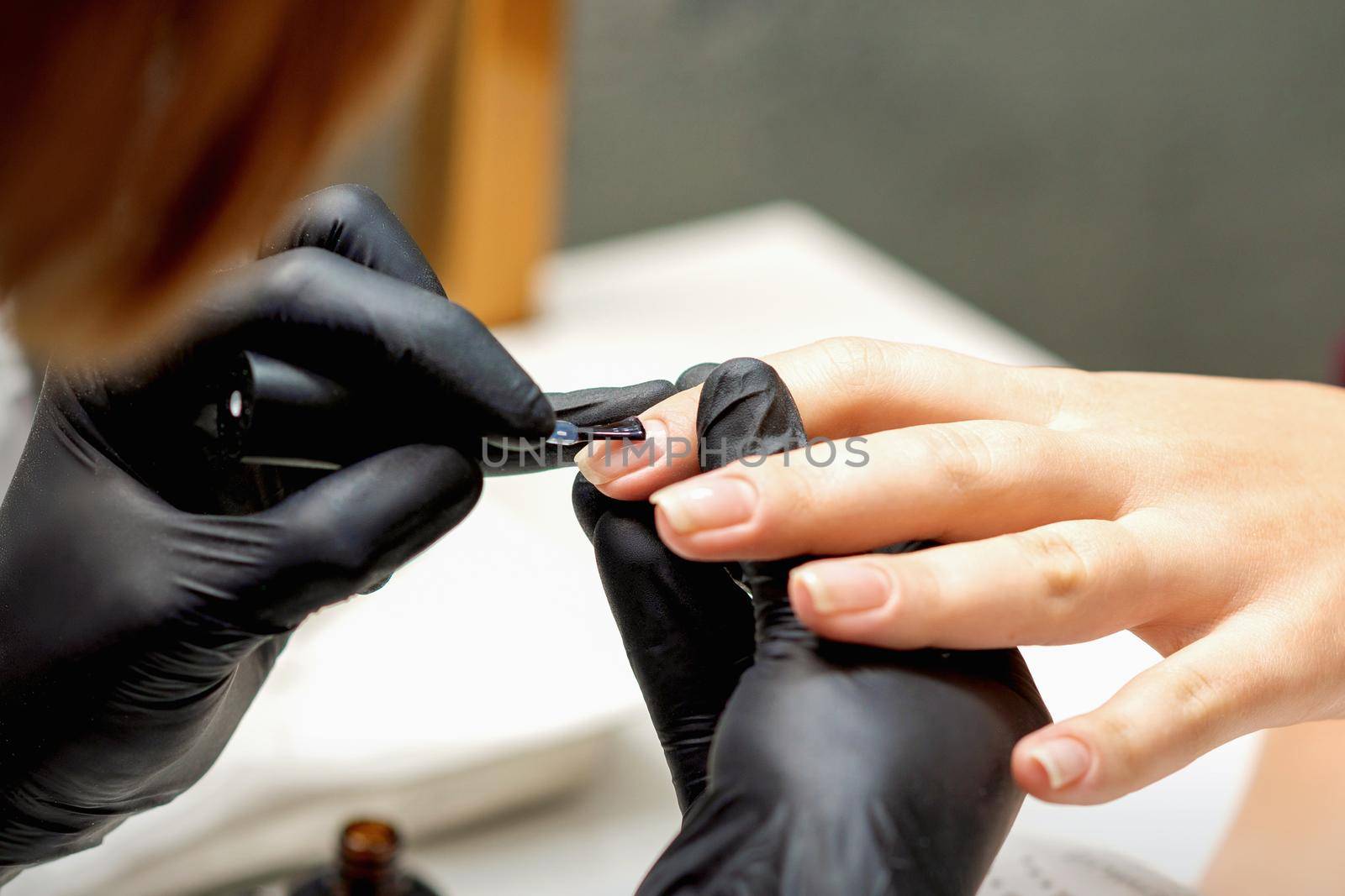 Close up of manicure master covering nails with the transparent polish of female nails in a nail salon