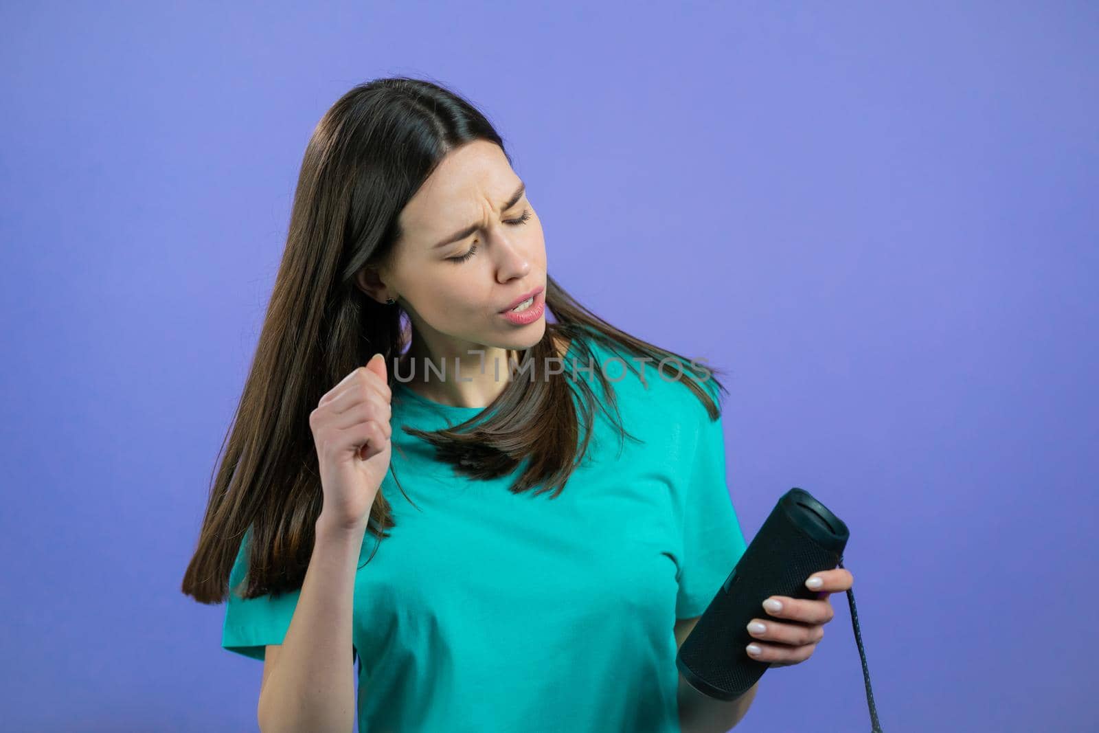 Woman listening to music by wireless portable speaker - modern sound system. Lady dancing, enjoying on violet studio background. She moves to the rhythm of music. High quality photo