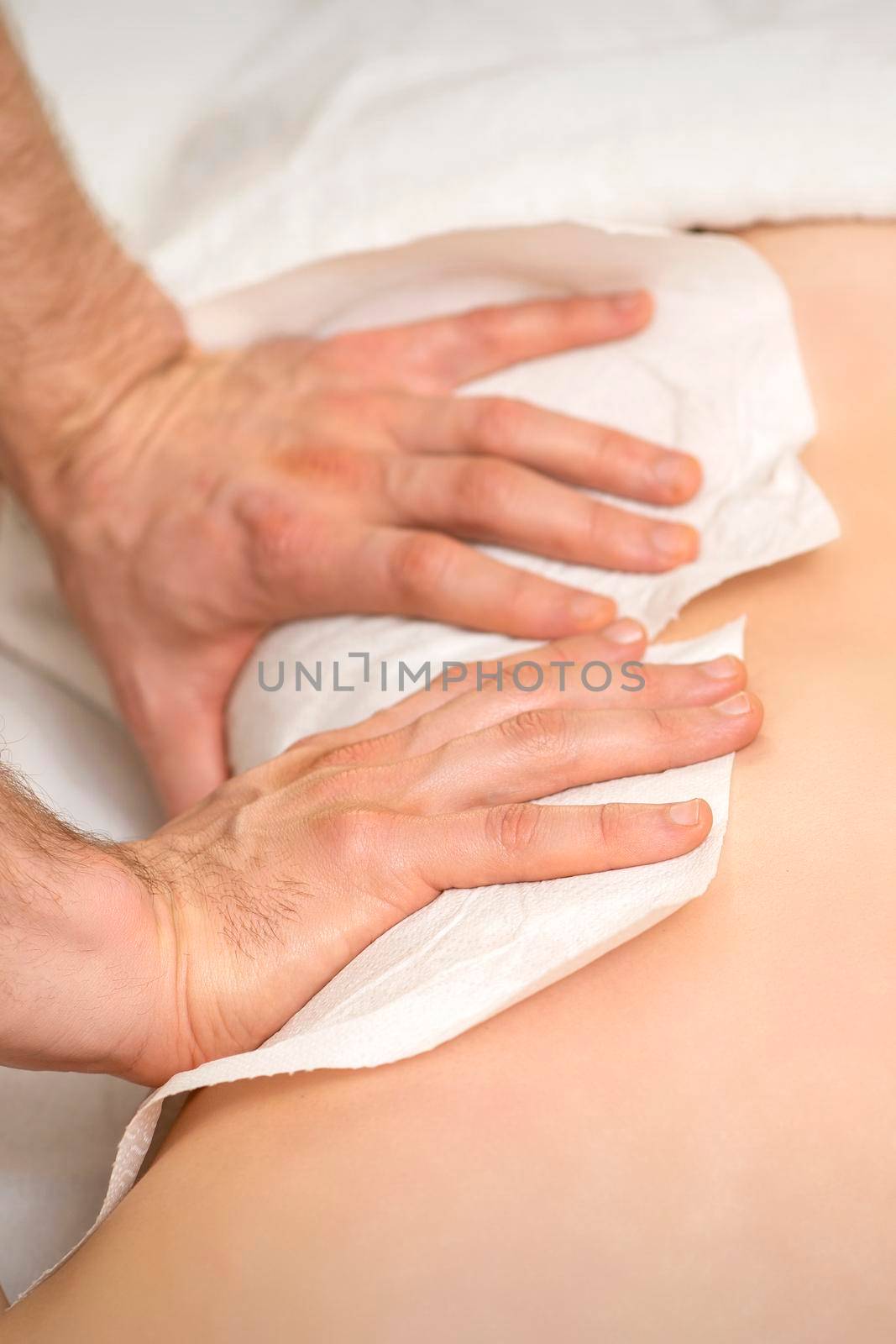Hands of a masseur with towel massaging back of a young adult woman in spa salon
