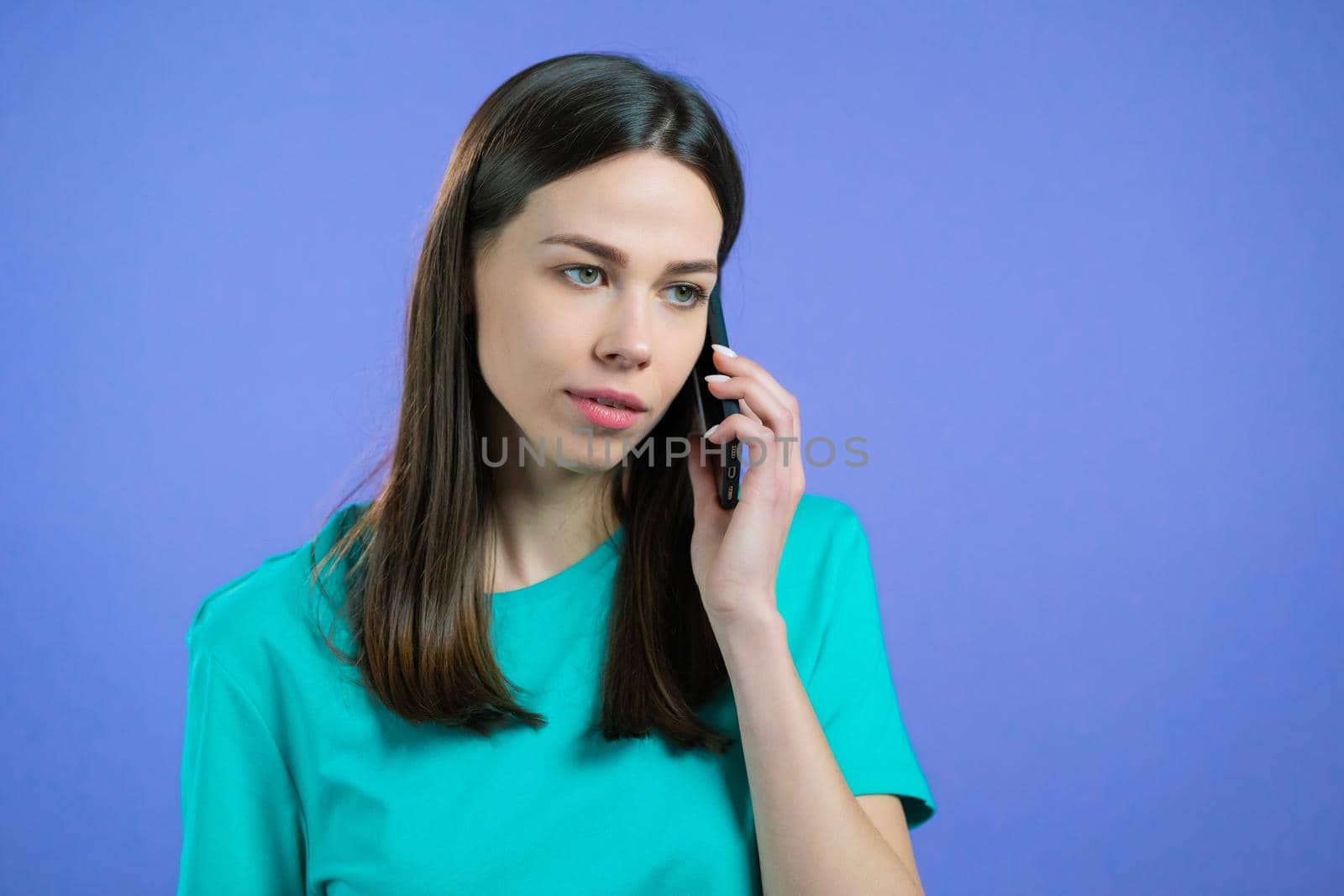Young woman speaks with smile on phone. Girl holding and using smart phone. Violet studio background. High quality photo