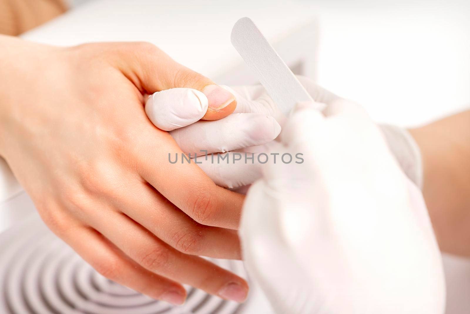 Manicure master wears white gloves with nail file doing manicure on female fingernails in a nail salon