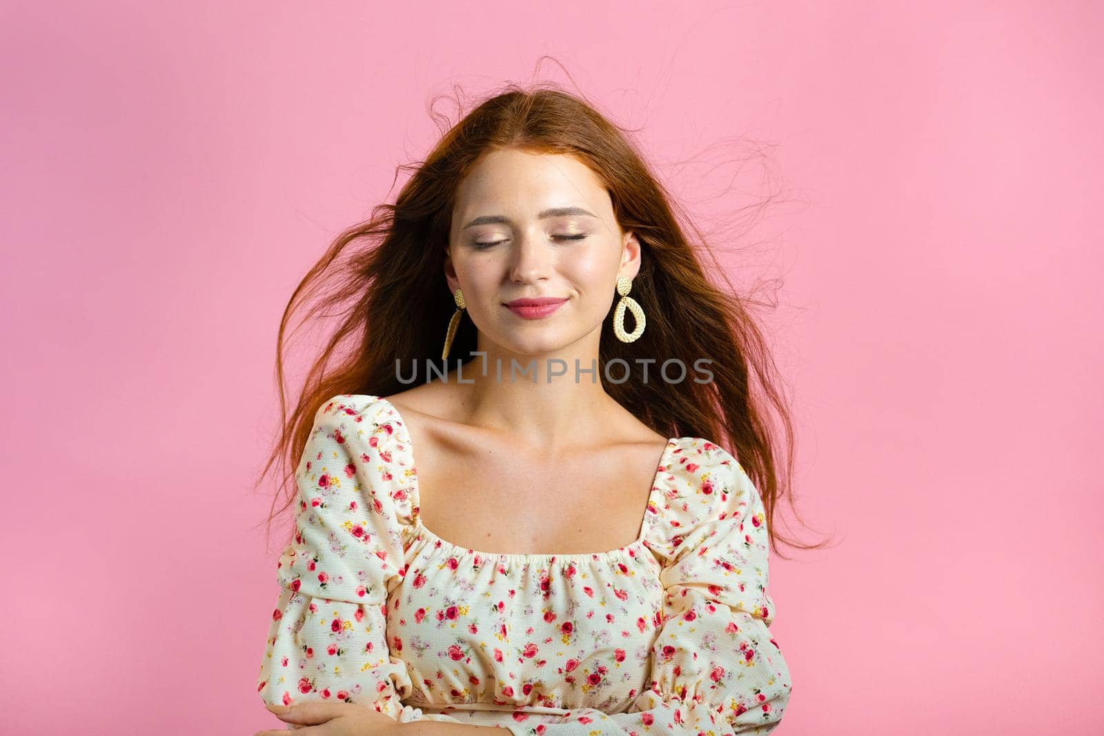 Young woman with long red wavy and shiny hairstyle looking to camera, flirting. Beautiful model girl demonstrate her elegant volume hair. Pink studio background. by kristina_kokhanova