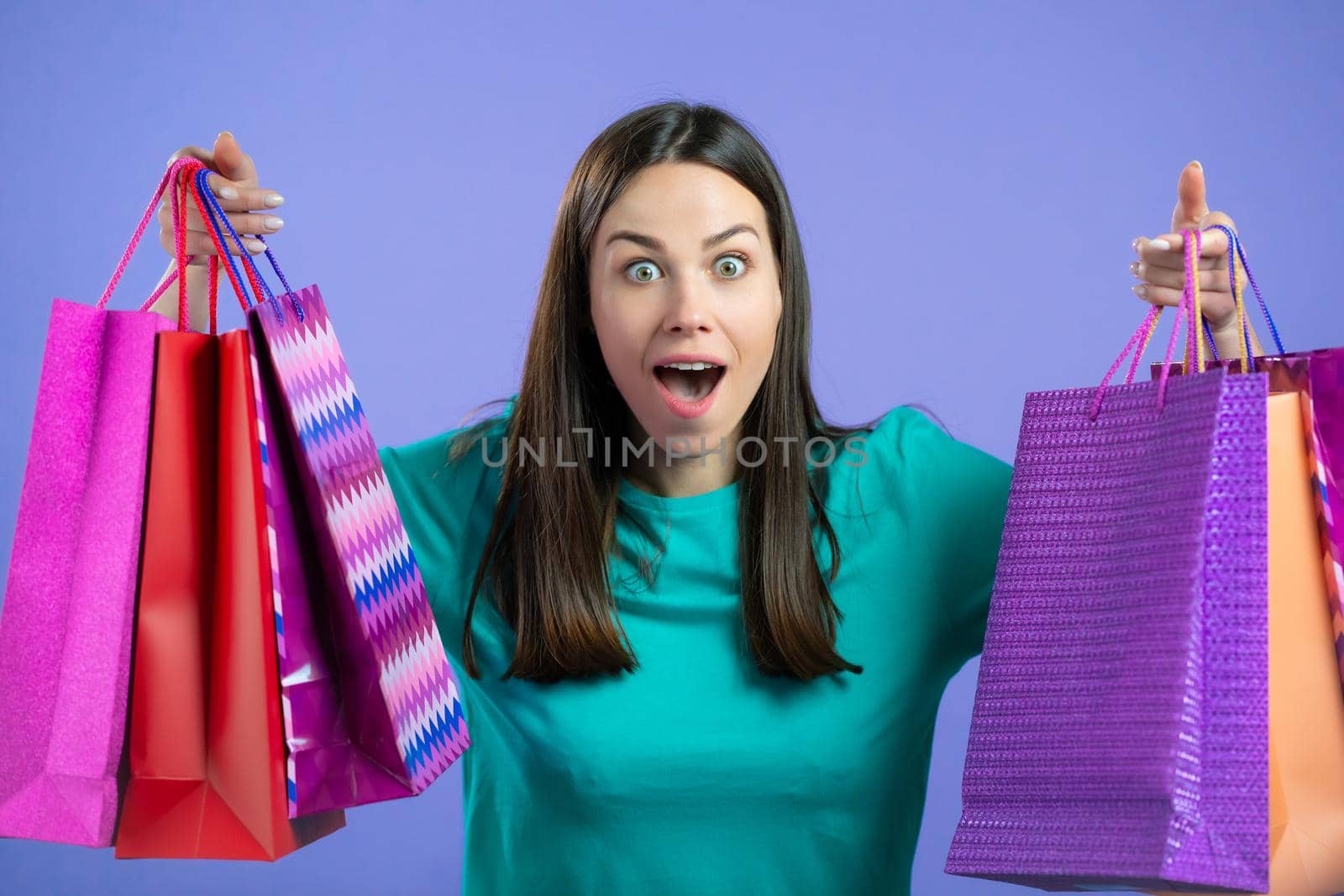 Excited woman with colorful paper bags after shopping on violet studio background. Concept of seasonal sale, purchases, spending money on gifts. High quality photo