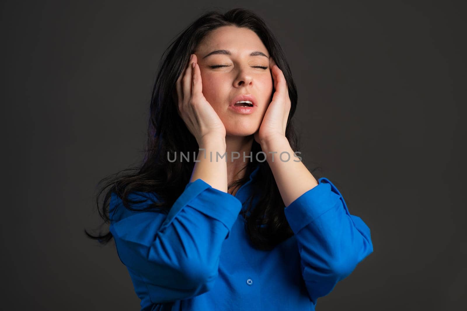 Bored mature woman with long hair having headache, studio portrait. Girl putting hands on head, isolated on grey background. Concept of problems and headache