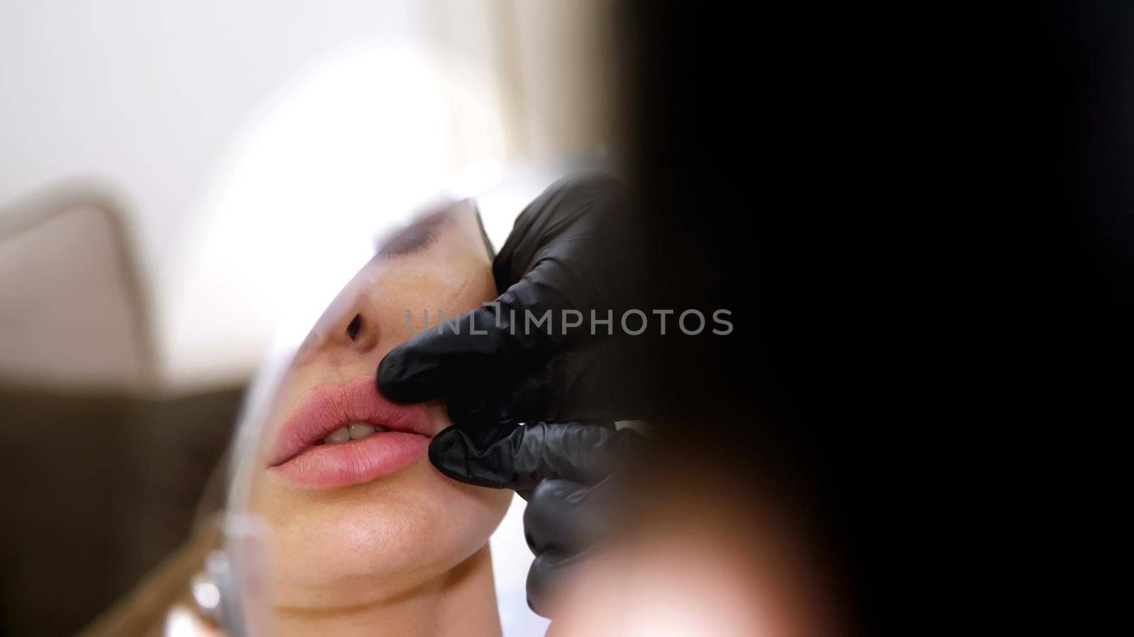 medical office, beautiful woman looking in the mirror, doctor probes the patient's lips after injections of hyaluronic acid into lips, correction of the shape of the lips. High quality photo