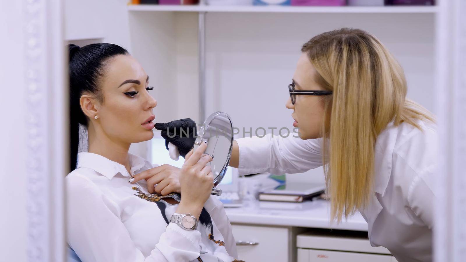 clinic, cosmetology room, the doctor shows the patient a lip zone for injection of hyaluronic acid, discuss the procedure of lip augmentation by djtreneryay